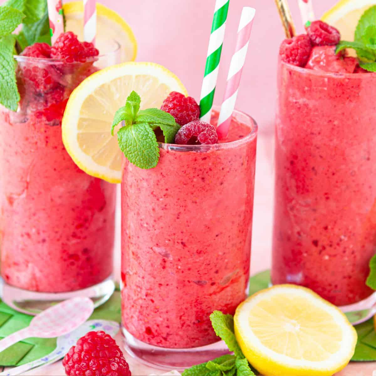 Three glasses of fruit cocktail drink garnished with mint leaves, raspberries and lemon slices.