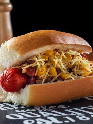 A Brazilian hot dog loaded with toppings on a table.