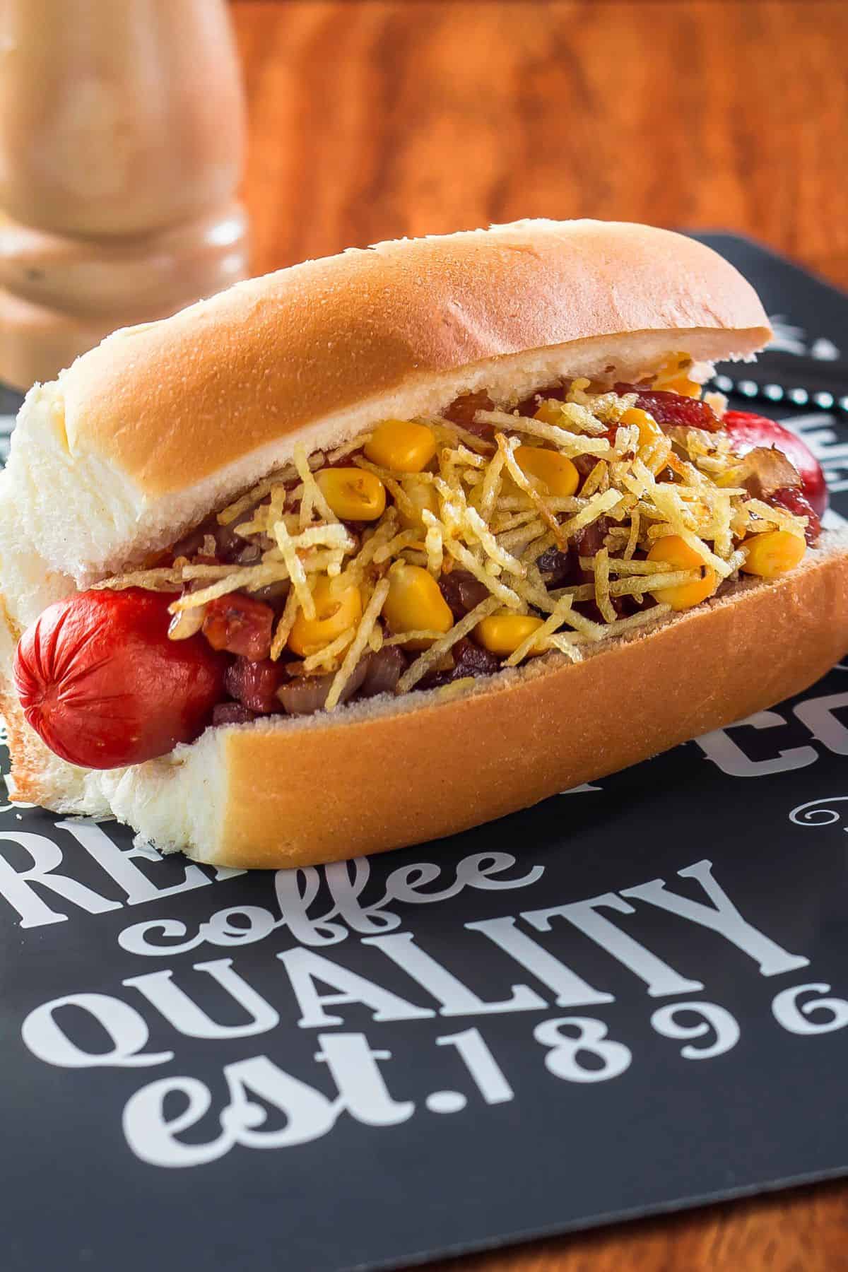Close up of a Brazilian hot dog with toppings on a table. 