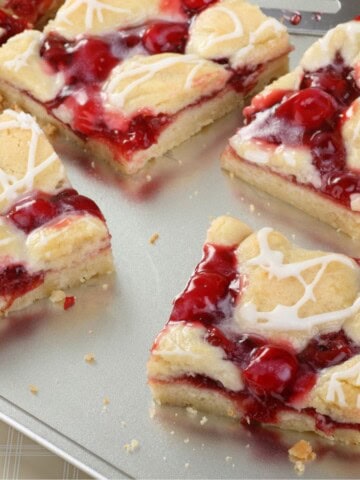 Several cherry bars drizzled with a white chocolate glaze on a baking sheet.