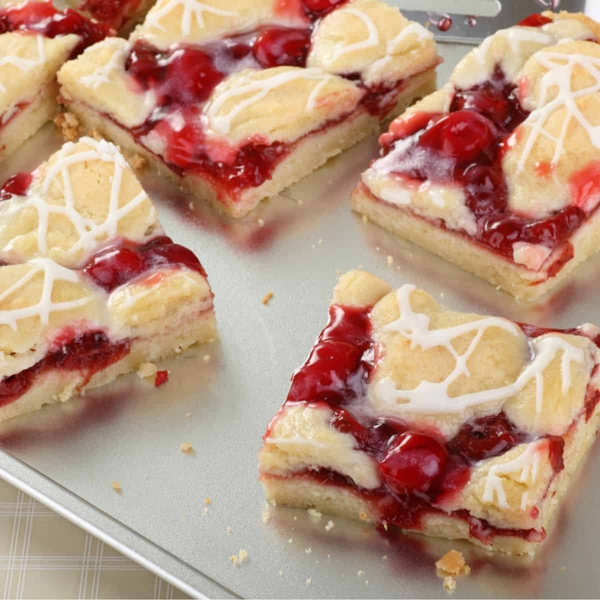 Several cherry bars drizzled with a white chocolate glaze on a baking sheet.