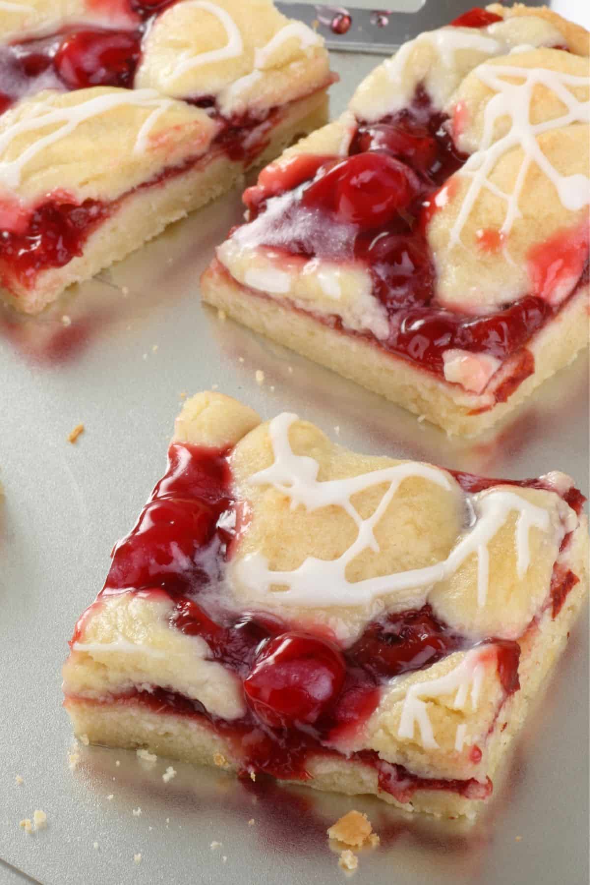 Several cherry dessert bars drizzled with melted white chocolate on a baking sheet.