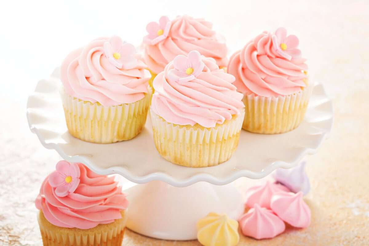 A cake stand with several baked goods witha pink frosting.