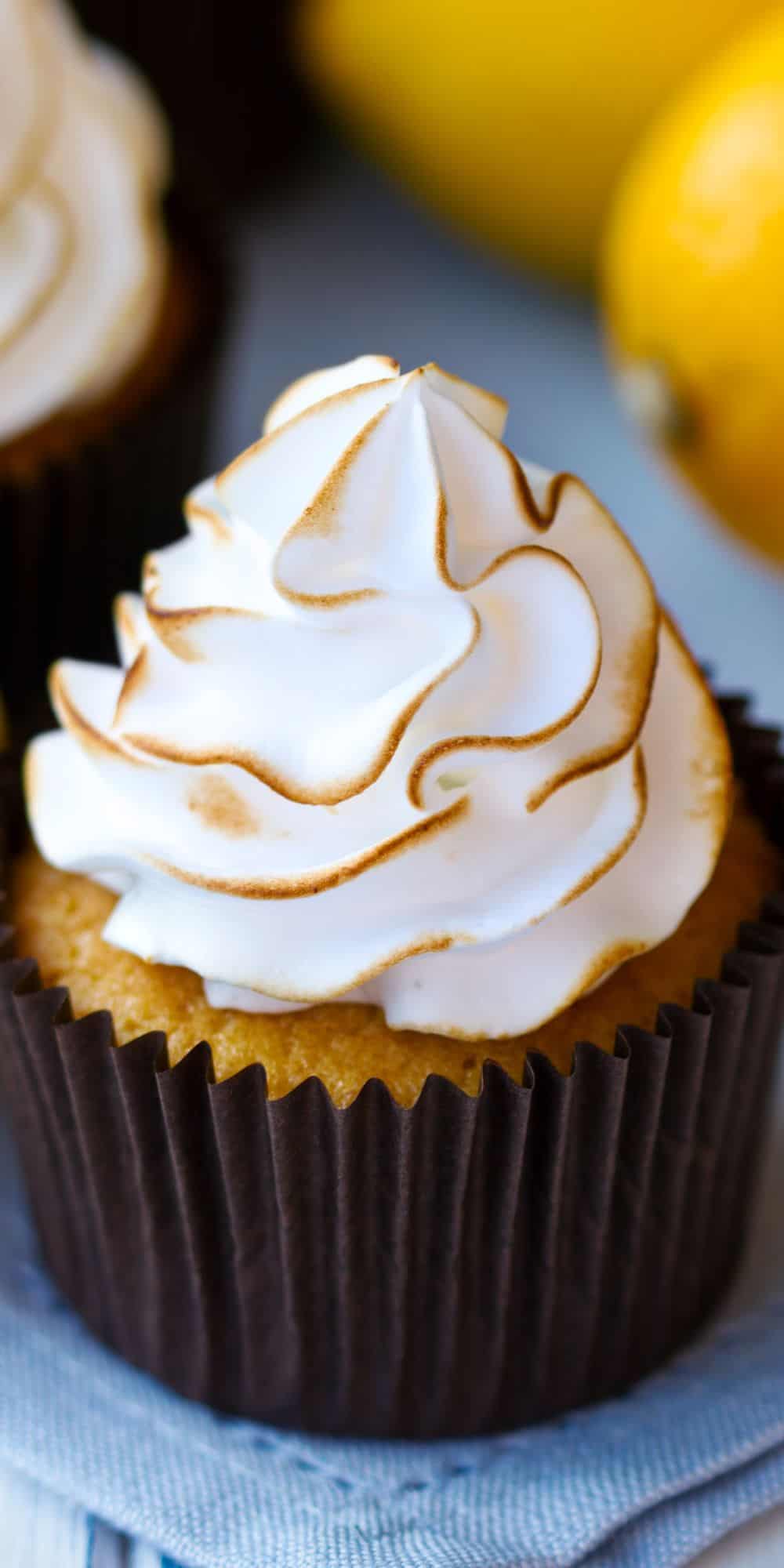 Close up of one lemon meringue cupcake with some lemons on the background. 