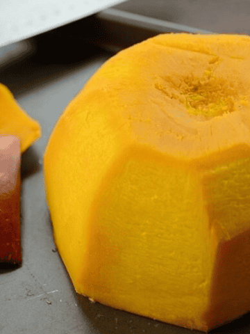 A peeled pumpkin cut in half in a tray with a knife on the side.