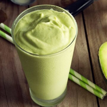 A tall glass of an avocado smoothie with straws on the side.