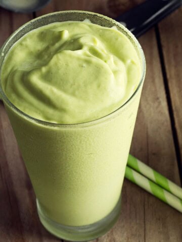 A tall glass of an avocado smoothie with straws on the side.