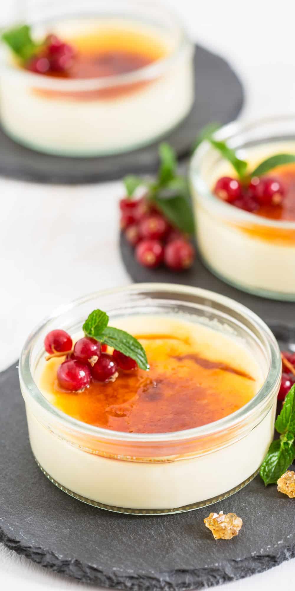 Two ramekins of coconut creme brulee garnished with fresh currants and mint leaves.