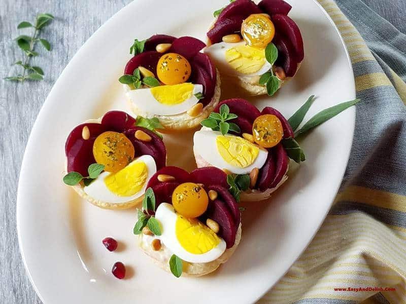 close up of a plate of puffy pastry tartlets with pickled beets, boiled eggs, and goat cheese on top