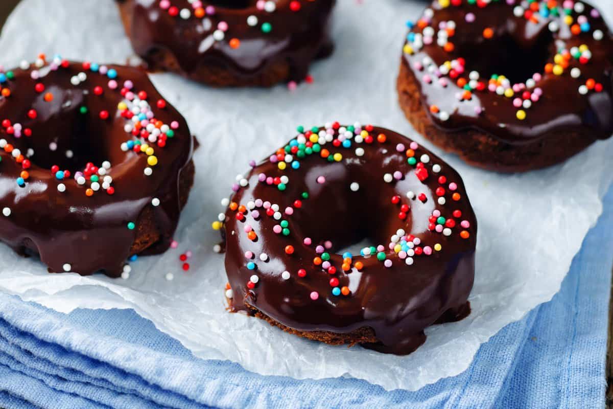 Frosted chocolate protein donuts with sprinkles on a parchment paper.