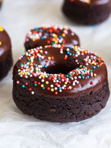 Close up of a chocolate protein donut with Nutella and funfetti sprinkles and a few other donuts on the background.