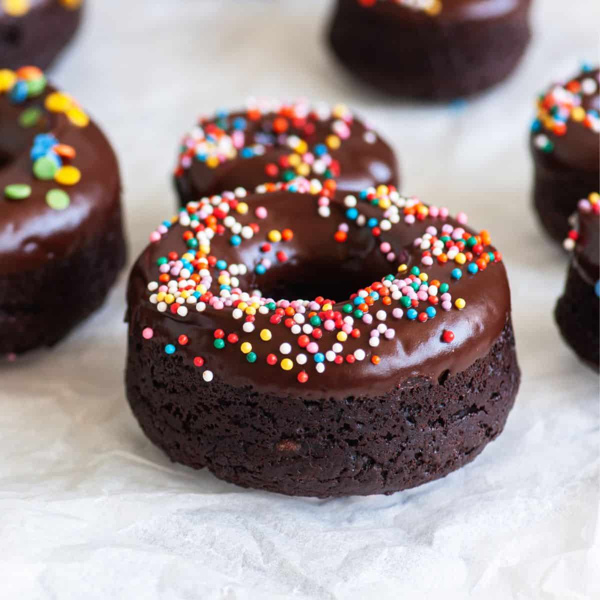 Close up of a chocolate protein donut with Nutella and funfetti sprinkles and a few other donuts on the background.