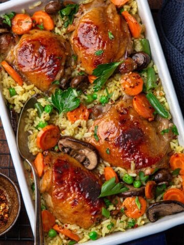 Sobrecoxas de frango assadas com legumes e grãos em assadeira.