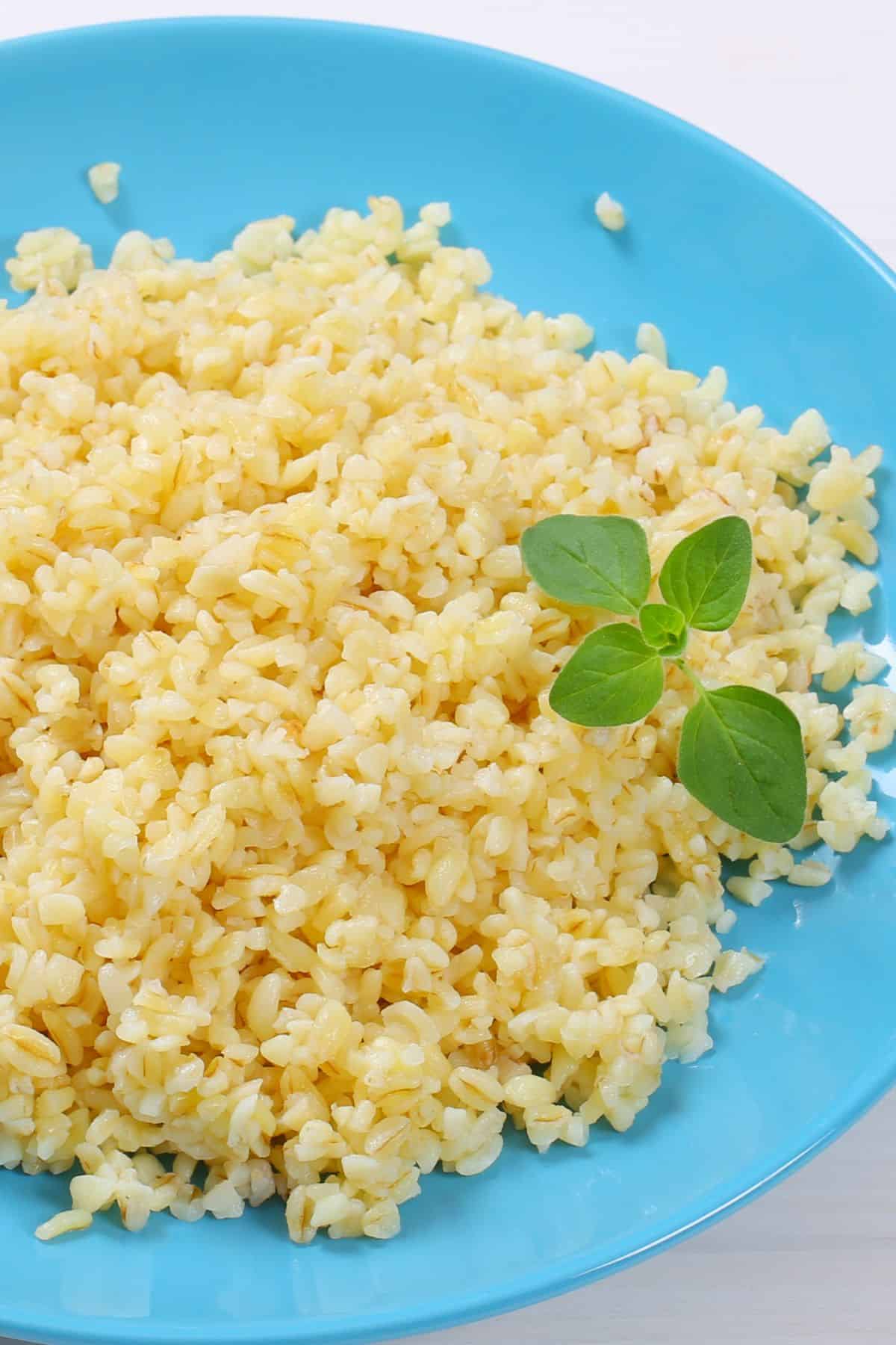 A plate of cooked pearled barley with some fresh herb on the side. 